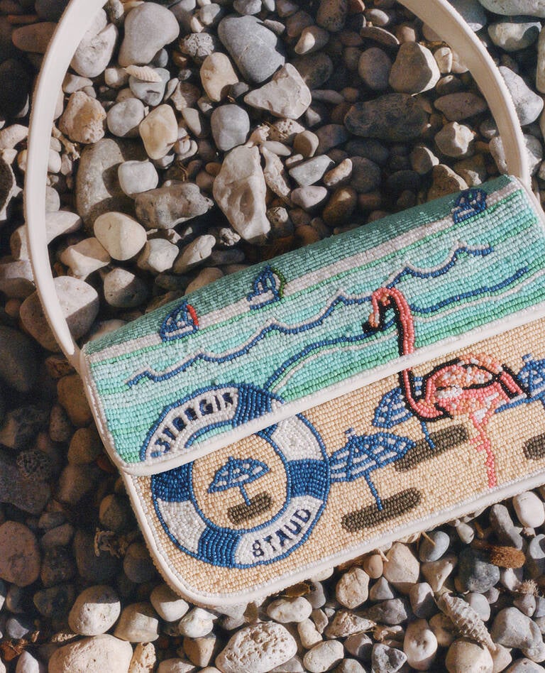 Decorative beaded Staud for St. Regis bag resting on beach pebbles Decorative beaded Staud for St. Regis bag resting on beach pebbles