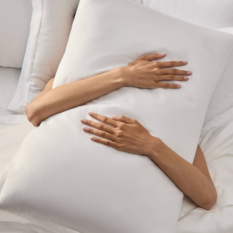 Woman hugging Marriott Bonvoy Boutiques plush pillow in bed
