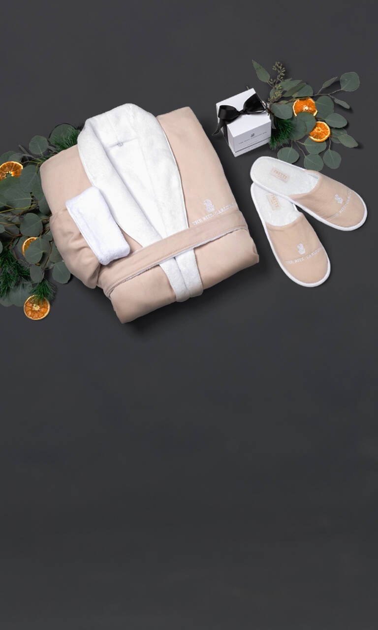 The Ritz-Carlton robe, slippers, and gift candle with scattered eucalyptus leaves and dried orange slices